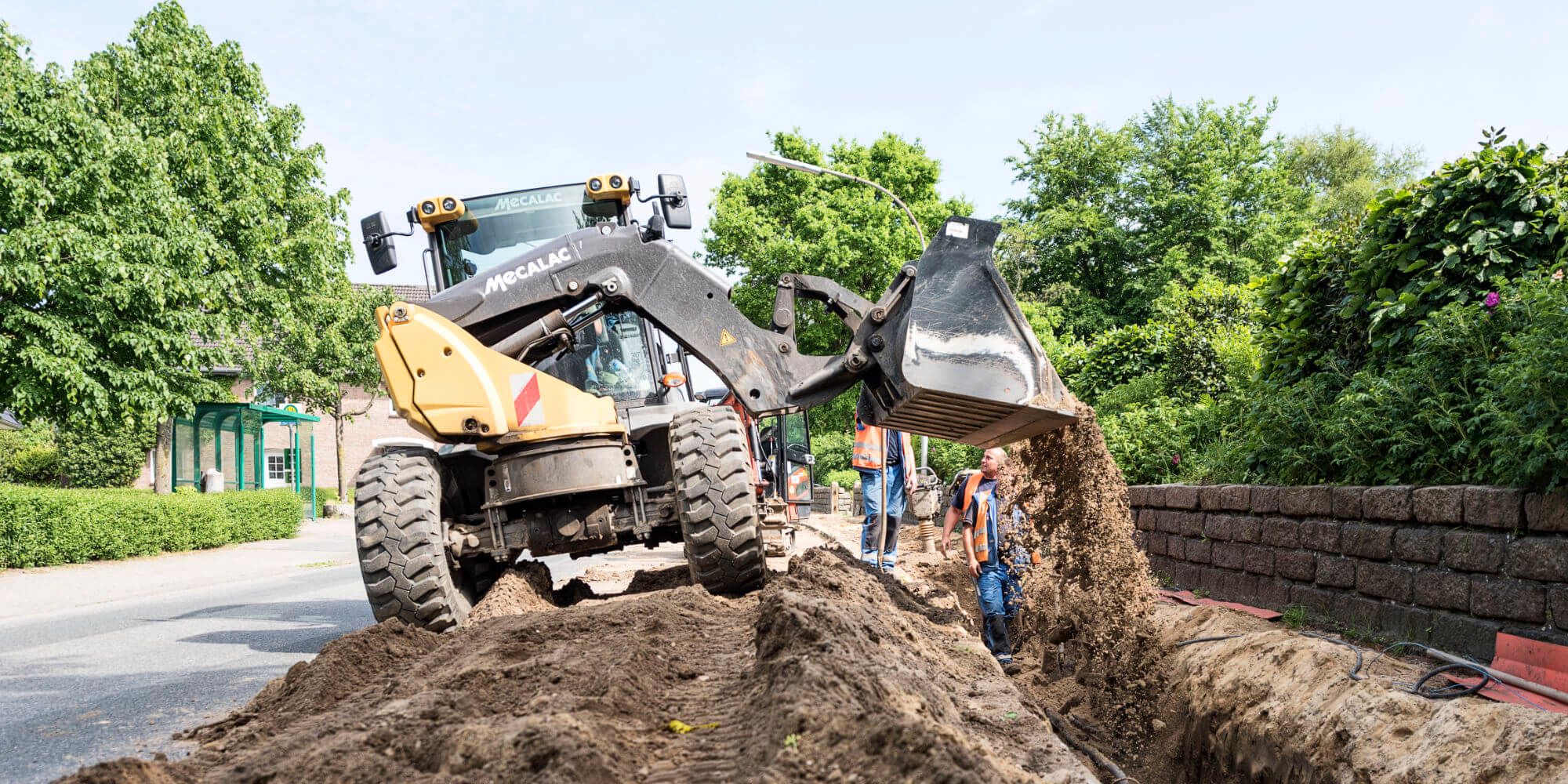 Mehrere Mitarbeiter und Bagger auf einer Baustelle, auf der ein Graben zugeschüttet wird